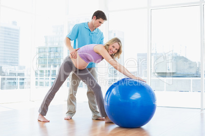 Trainer exercising with smiling pregnant client and exercise bal