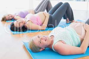 Happy pregnant women in yoga class lying on mats
