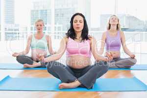 Meditating pregnant women in yoga class sitting on mats