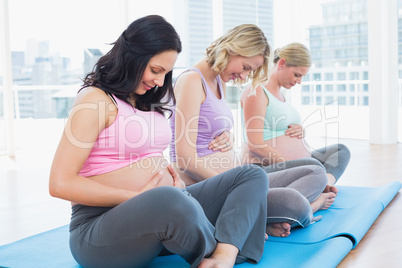 Happy pregnant women sitting in yoga class touching their bumps