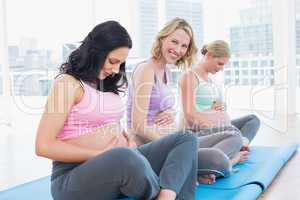 Smiling pregnant women sitting in yoga class touching their bump