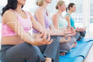 Calm pregnant women meditating in yoga class