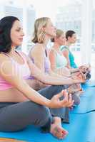 Content pregnant women meditating in yoga class