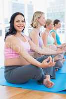 Content pregnant women meditating in yoga class with one smiling
