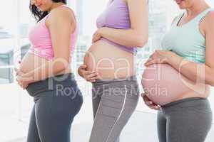 Pregnant women standing in a row looking at bumps