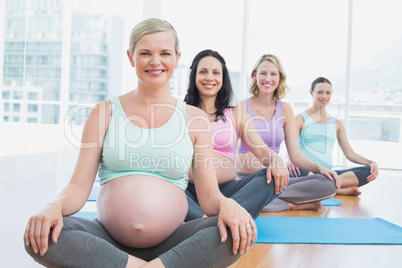 Happy pregnant women in yoga class sitting on mats