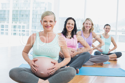 Pregnant women in yoga class sitting on mats touching their bump