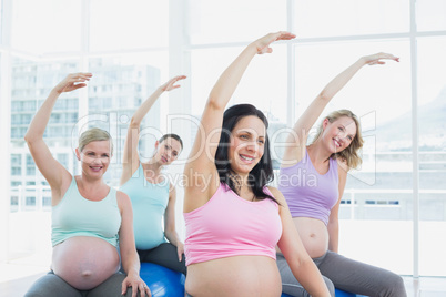 Happy pregnant women sitting on exercise balls stretching arms
