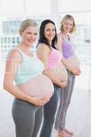 Cheerful pregnant women standing in a line smiling at camera
