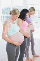 Cheerful pregnant women standing in a line smiling at bumps