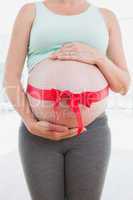 Pregnant woman standing with red bow around belly