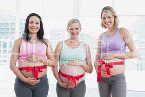 Happy pregnant women standing with red bow around bumps