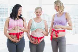 Smiling pregnant women standing with red bow around bumps