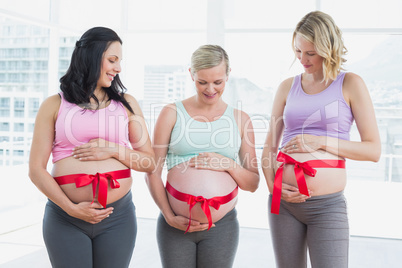 Cheerful pregnant women standing with red bow around bumps