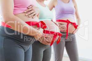 Pregnant women standing with red bow around bumps
