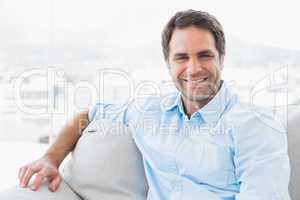 Smiling handsome man sitting on the couch looking at camera