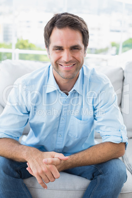 Happy handsome man sitting on the couch looking at camera