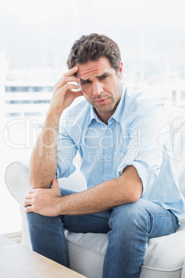 Man with headache sitting on the couch looking at camera