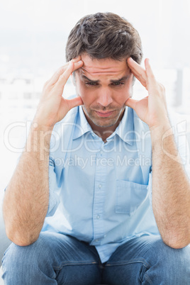 Wincing man with headache sitting on the couch