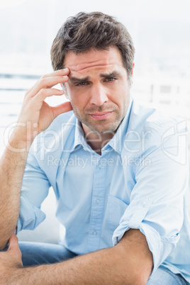 Wincing man with headache sitting on the couch looking at camera