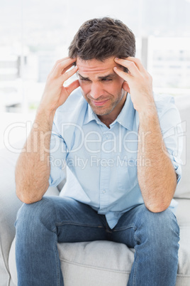 Grimacing man sitting on the couch with a headache