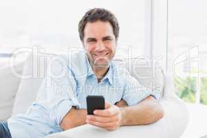 Smiling man sitting on the couch sending a text