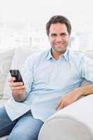Smiling man sitting on the couch sending a text with smartphone