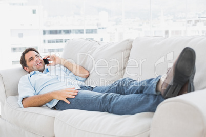 Happy man lying on the couch talking on the phone