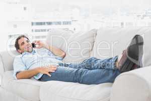 Happy man lying on the couch talking on the phone