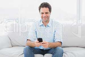 Happy man sitting on the couch sending a text message