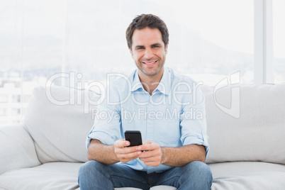 Cheerful man sitting on the couch sending a text message