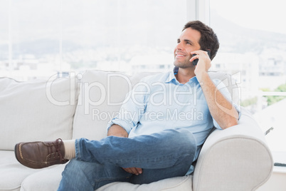 Cheerful man sitting on the couch making a phone call