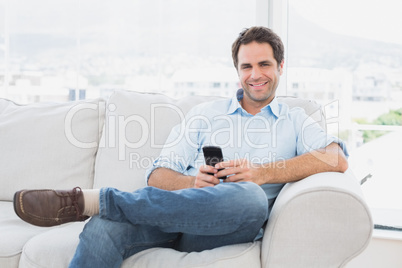 Happy man sitting on the couch using his smartphone Happy man sitting on the couch using his smartphone