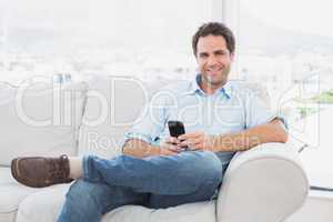 Happy man sitting on the couch using his smartphone