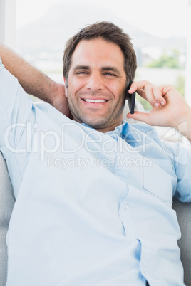 Happy man sitting on the couch on the phone smiling at camera