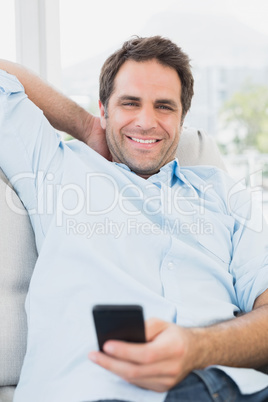 Smiling man sitting on the sofa texting on his phone looking at