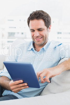 Handsome happy man sitting on the sofa using his tablet pc