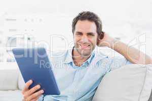 Handsome man sitting on the sofa using his tablet pc smiling at
