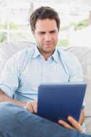 Focused man sitting on the couch using his tablet