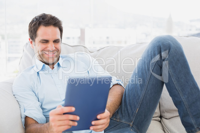Smiling man relaxing on the couch using his tablet Smiling man relaxing on the couch using his tablet