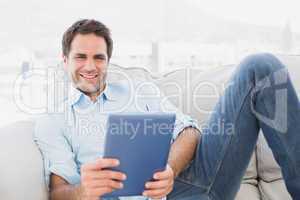 Happy man relaxing on the couch using his tablet