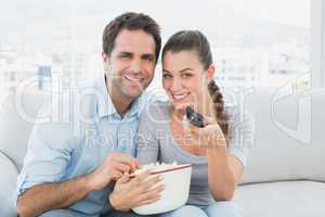 Smiling couple watching tv on the couch with bowl of popcorn