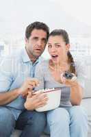 Couple watching scary movie on the sofa with bowl of popcorn
