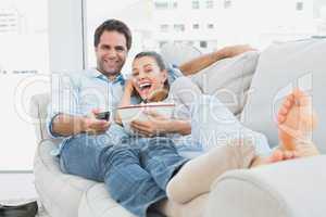 Couple watching funny movie lying on the sofa with bowl of popco