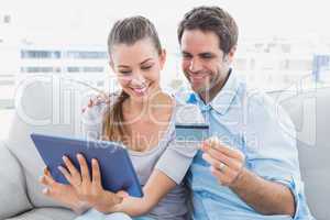 Happy couple relaxing on the couch shopping online with tablet p