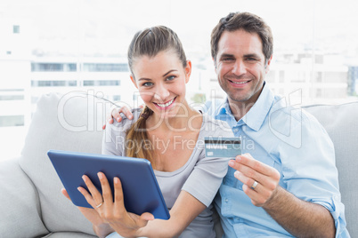 Happy couple sitting on the couch shopping online with tablet pc