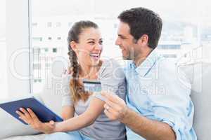 Laughing couple sitting on the couch shopping online with tablet