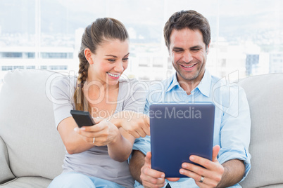 Happy couple sitting on the couch using tablet pc and watching t