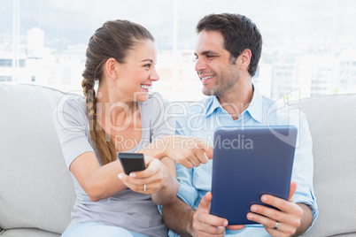 Smiling couple sitting on the couch using tablet pc and watching