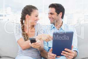 Smiling couple sitting on the couch using tablet pc and watching
